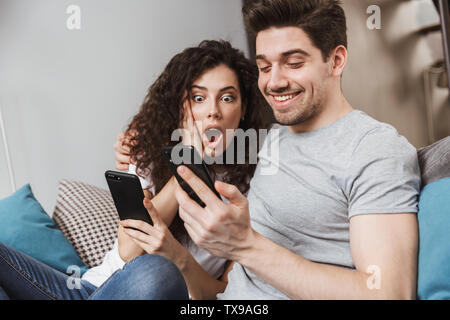 Bild der kaukasischen junges Paar, Mann und Frau 30 s auf dem Sofa zu Hause sitzt und mit Smartphones zusammen Stockfoto
