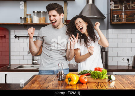 Portrait von freundlichen Paar Mann und Frau 30s Musik zusammen beim Kochen Salat in der Küche zu Hause. Stockfoto