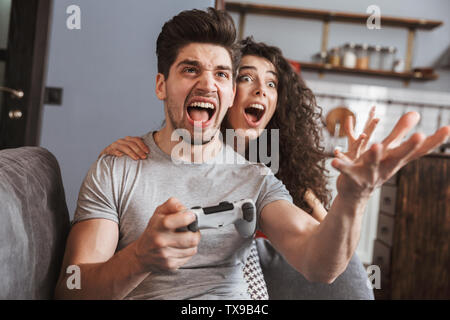 Bild von Angeregten Paar Mann und Frau 30 s auf dem Sofa zu Hause sitzen und Spielen von Videospielen zusammen mit Joysticks Stockfoto