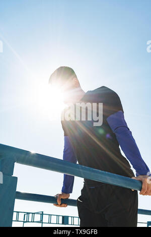 Foto von jungen Kerl 20 s in schwarz Trainingsanzug, Akrobatik auf horizontale Gymnastik bar während der morgendlichen Workout von Seaside Stockfoto