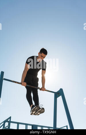 Foto der jungen Sportler 20 s in schwarz Trainingsanzug, Akrobatik auf horizontale Gymnastik bar während der morgendlichen Workout von Seaside Stockfoto