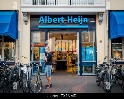 Haarlem, Niederlande - 20.August 2018: Vorderansicht des Albert Heijn niederländische Supermarktkette, 1887 in Oostzaan, Niederlande, gegründet auf Kruisstraat 10 Straße mit jungen Mann essen eine Schokolade außerhalb Stockfoto