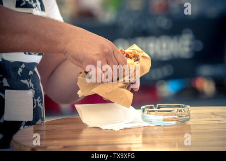 Der Mann hält in der Hand und isst Hamburger. Sommer in ein Restaurant im Freien. verschwommenen Hintergrund. Stockfoto