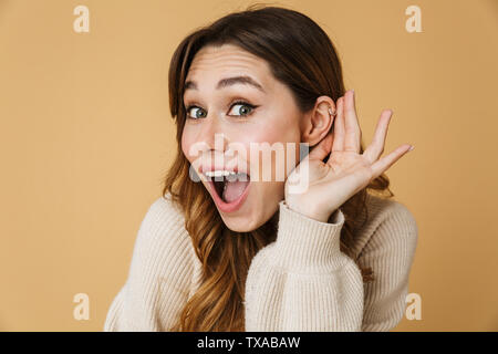 Schöne junge Frau trug Pullover stehend über beigen Hintergrund isoliert, versucht, Gerüchte zu hören Stockfoto