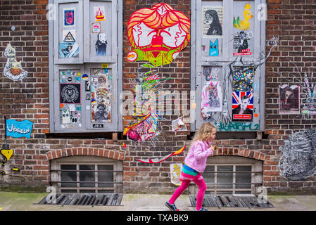 Brick Lane, Shoreditch, London, England, UK: der kleine blonde Junge Mädchen in Brick Lane in der Nähe einer Wand in Graffiti Wandbild street art abgedeckt Stockfoto