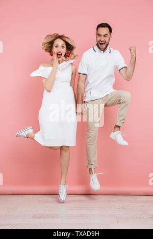 Die volle Länge eines glücklichen schönes Paar in Liebe über rosa Hintergrund isoliert springen, Feiern Stockfoto