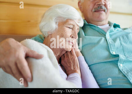 Liebenswürdige Oma mit weißem Haar nickerchen an der Schulter der Ehegatten Stockfoto