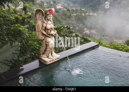 Flanke von privaten Infinity Pool mit verzierten Brunnen als Balinesen Statue des Engels. Jungle View in Ubud, regnerischen Wetter Stockfoto