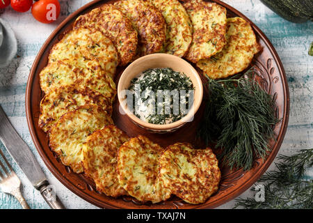 Zucchini Krapfen werden auf eine Platte gelegt, in der Mitte gibt es saure Sahne Sauce mit Knoblauch und Dill, horizontale Foto Stockfoto