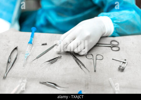 Chirurgen Hand, Scheren, Pinzetten, chirurgische Instrumente auf dem Tisch für den Betrieb Arbeiten im Betrieb Zimmer im Krankenhaus, Notfall, Stockfoto