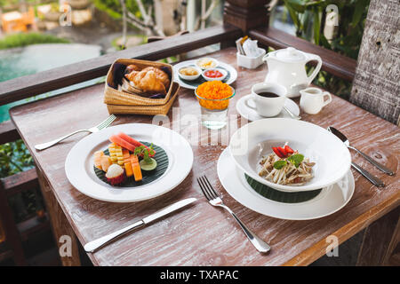 Frühstück mit balinesischen Obstteller, Körbchen mit Croissants und Obst Salat auf hölzernen Tisch Stockfoto