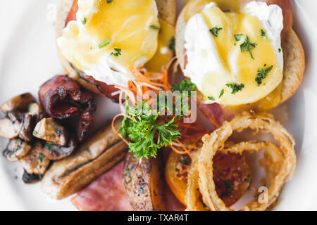 Eier Benedikt mit Zwiebelringen, Würstchen, Baked Potato und gebratenen Champignons auf weißem Hintergrund Top View close-up Stockfoto