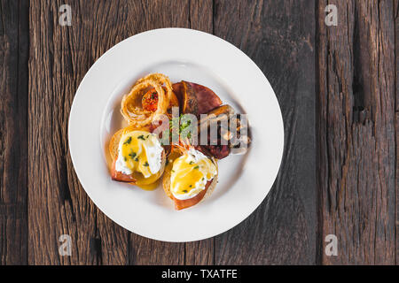 Eier Benedikt mit Zwiebelringen, Würstchen, Baked Potato und gebratene Pilze an Holz- Hintergrund der Ansicht von oben Stockfoto