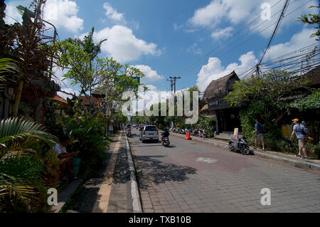 Ubud, Bali, Indonesien - 12. April 2019: Street View der Jalan Raya Ubud-Straße an einem sonnigen Tag mit Menschen, Motorräder und Autos fahren Stockfoto