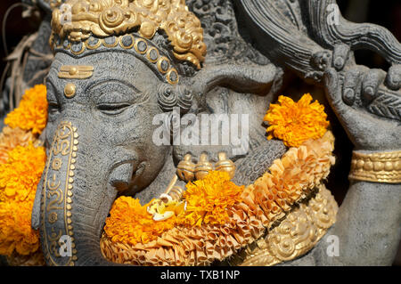Seite Kopf geschossen von einem schönen Ganesha Stein Statue mit Ringelblume Blumen dekoriert und vor einem Spa Eingang in Ubud, Bali - Indonesien Stockfoto