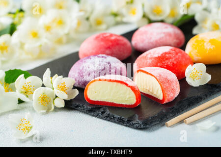 Mehrfarbige Japanische ice cream Mochi Reis Teig und Jasminblüten auf einer konkreten blauen Hintergrund. Traditionelle japanische Dessert auf schwarzem Schiefer. Stockfoto