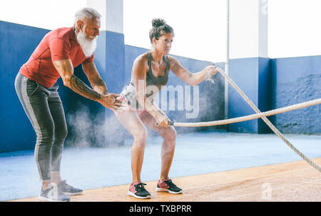 Passende Frau Training mit Schlacht Seil im Fitnessstudio - Hipster personal trainer Motivieren einer weiblichen Athleten wer tut Ausdauerübungen Stockfoto