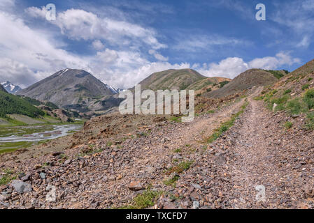 Rocky Feldweg hoch in die Berge und einen Blick von oben auf das Tal und den Fluss auf dem Hintergrund der blauen Himmel mit Wolken Stockfoto