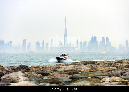 (Selektive Fokus) ein kleines Boot mit Touristen an Bord Segeln vor der Skyline von Dubai von einer dicken Morgens Nebel umgeben. Dubai, VAE. Stockfoto