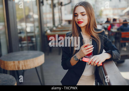 Stilvolle Frau in einem Cafe. Dame mit Telefon. Modische Mädchen in einer schwarzen Jacke. Famale trinken Saft Stockfoto