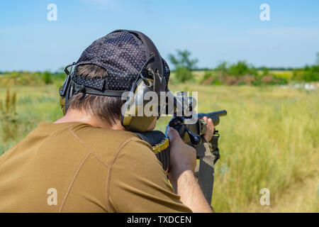 Der Shooter in einem braunen T-Shirt und eine Baseballmütze zielt darauf ab, ein Gewehr Stockfoto