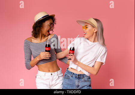 Charkow, Ukraine - April 01, 2019: Tausendjährigen Frauen genießen Coca-Cola Classic mit Stroh auf rosa Hintergrund. Das Getränk wird produziert und hergestellt, b Stockfoto