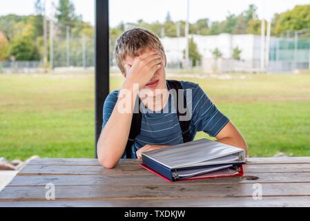 Gelangweilte Teenager ungern seine Hausaufgaben zu machen, während an einem Tisch sitzen. Stockfoto