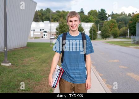 Gerne männliche Teenager stehen auf dem Bürgersteig neben einer Schule mit seinem Bindemittel. Stockfoto