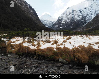 Ein Strom fließt durch ein Tal zwischen weißen, schneebedeckten Berge Stockfoto