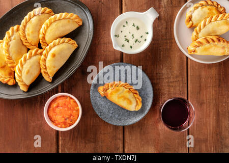 Empanadas mit Saucen und Wein, geschossen von oben auf einen dunklen Holzmöbeln im Landhausstil Hintergrund Stockfoto