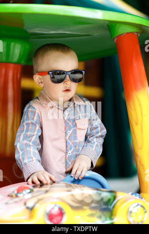 Kleinen Niedlichen Jungen ist in Spaß beim Spielen auf einem großen spielzeugauto Stockfoto