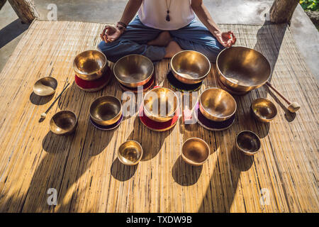 Frau spielen auf Tibetische Klangschale sitzend auf Yoga Matte gegen einen Wasserfall. Vintage tonned. Schöne Mädchen mit mala Perlen meditieren Stockfoto