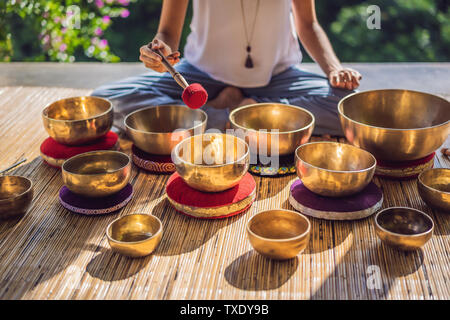 Frau spielen auf Tibetische Klangschale sitzend auf Yoga Matte gegen einen Wasserfall. Vintage tonned. Schöne Mädchen mit mala Perlen meditieren Stockfoto