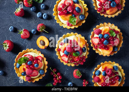 Schönen Sommer köstliche Torten mit frischen Pudding cremige Füllung gekrönt mit Himbeeren, Aprikosen, Heidelbeeren, Erdbeeren, rote Johannisbeeren auf eine konkrete Stockfoto