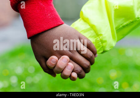 Zwei Kinder von verschiedenen Rassen die Hände zusammen. Foto zeigt Freundschaft, Gleichheit und Vielfalt. Eine Kaukasische der Anderen ist dunkel (schwarz). Stockfoto