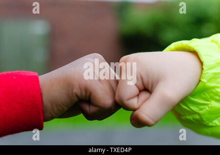 Zwei Kinder verschiedener Rassen und Hautfarben Begrüßung mit Faust stoßen. Foto zeigt Freundschaft, Unterstützung, Gleichheit und Vielfalt. Stockfoto