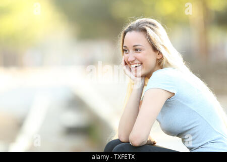 Happy teenage Mädchen lachen weg schauen sitzt in einem Park mit Kopie Raum Stockfoto