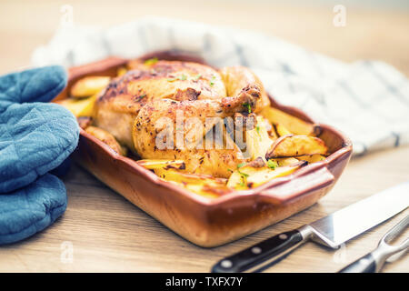 Gebratene ganze Hähnchen mit Kartoffeln, in Auflaufform. Leckeres Essen zu Hause auf dem Küchentisch Stockfoto