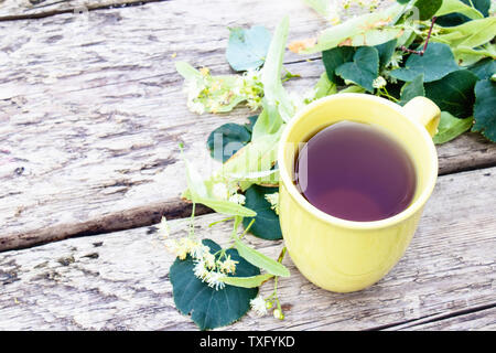 Linden Tee in eine gelbe Schale steht in der Nähe von Linden Blumen vor dem Hintergrund des alten Boards. Kräutertee mit Linden Blumen. Stockfoto