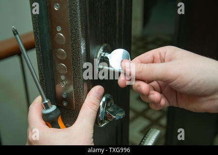 Mann zur Festsetzung der Tür mit einem Schraubendreher. Türschloss reparieren. Stockfoto