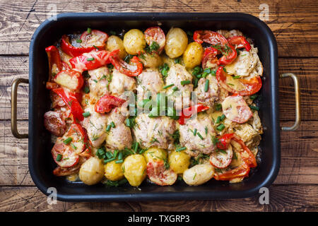 Gebackene Hühnerkeule, Kartoffeln und Gemüse in ein Backblech auf einem Holztisch Stockfoto