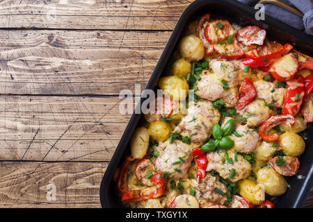 Gebackene Hühnerkeule, Kartoffeln und Gemüse in ein Backblech auf einer hölzernen Tabelle kopieren. Stockfoto