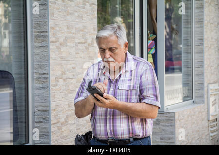 Belgrad, SERBIEN - Juli 14, 2015: Alte älterer weißer Mann stehen und auf Smartphone verwirrt, seine Internet mobile Services Bild von o Zu verwenden Stockfoto