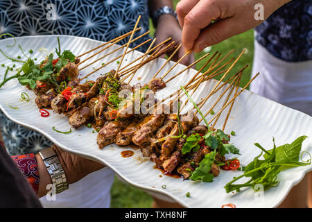 Sate Ayam, gegrilltem Hähnchenfleisch auf Holzspieße serviert mit Sambal kacang, Erdnuß-Sauce. Hände die Spieße. Indonesische Küche. Stockfoto