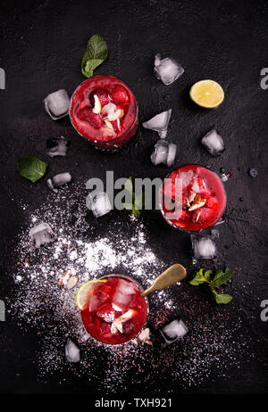 Blended strawberry shake Smoothie mit ganzen Erdbeeren, Eis und Zitrone in Gläsern und Eiswürfel auf schwarzem Hintergrund. Gesunde Ernährung Diät Konzept. Stockfoto