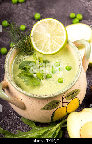 Grün creme Suppe der grüne Erbsen, Avocado, Rucola, Spinat, Minze, Limette, Dill, Petersilie. Smoothie Schüssel auf schwarzen Hintergrund. Stockfoto