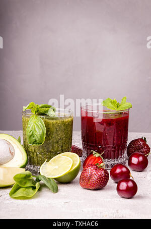 Grüne und rote Smoothie der Erdbeere, süße Kirsche, Avocado, Spinat, Basilikum, Kalk, green apple auf grauem Hintergrund. Gesunde Ernährung eatin Konzept. Stockfoto