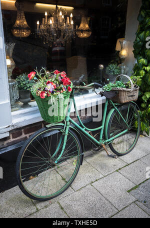 Eine alte vintage Bike angezeigte Blumenkörbe außerhalb ein Antiquitätengeschäft in Großbritannien. Stockfoto