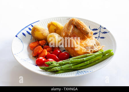 Im Ofen gebratenes Huhn mit Pflaumen Tomaten, neuen Kartoffeln und grünem Spargel auf einer Platte. Stockfoto