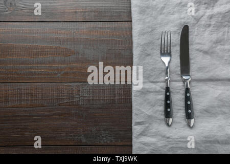 Rustikale schwarz Besteck mit Bettwäsche Handtuch auf braun Holzbrett. Ansicht von oben mit der Kopie Raum für Ihr Menü oder ein Rezept. Kochen Hintergrund. Stockfoto